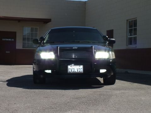 2003 Ford Crown Victoria - Direct front shot of a black sedan, billet grille and EVIL VIC plate, building behind.
