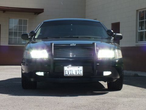 2003 Ford Crown Victoria - Front view of a black sedan; plate EVIL VIC with CROWN VICTORIA frame and grille guard.