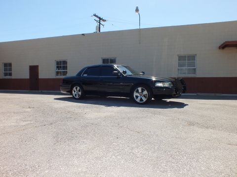 2003 Ford Crown Victoria - Right-side profile of a lowered black sedan on chrome wheels in a paved lot.