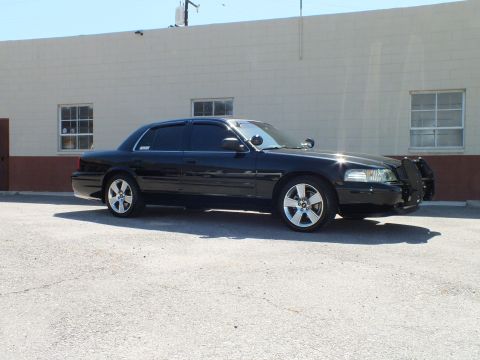 2003 Ford Crown Victoria - Side view of a black sedan, grille guard at front, parked against a cinderblock wall.