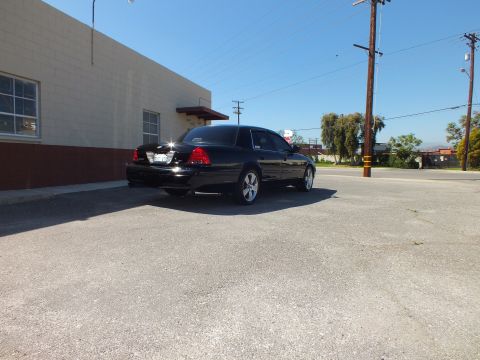 2003 Ford Crown Victoria - Rear-right angle of a black sedan in a paved lot with power lines and trees behind.
