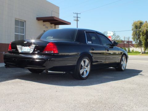 2003 Ford Crown Victoria - Rear-left view of a black sedan, EVIL VIC plate and chrome wheels beside a building.