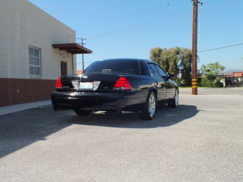 2003 Ford Crown Victoria - Rear angle of a black sedan with glowing taillights near a utility pole and trees.