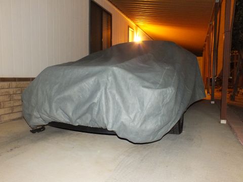 2003 Ford Crown Victoria - Gray car cover over a sedan-shaped vehicle parked in a lit narrow carport.