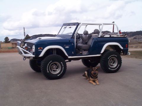 1977 Ford Bronco - Driver-side three-quarter view of a lifted blue topless, doorless early Ford Bronco with a white exterior roll cage, white fender flares, w…