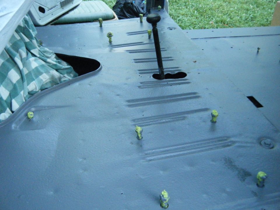 Vehicle floor with bolts and a gear shifter. Some cloth is covering part of the floor