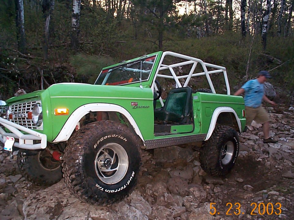 Green 1977 Ford Bronco with white roll cage on rocky terrain