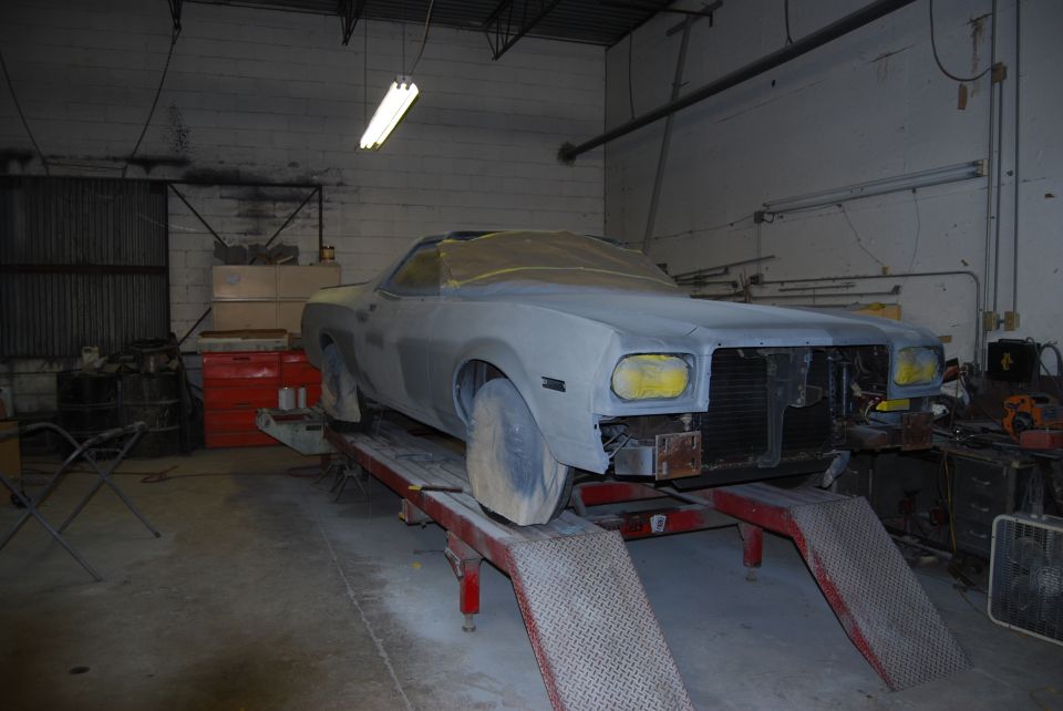1975 Ford Ranchero in primer on a lift, front end exposed