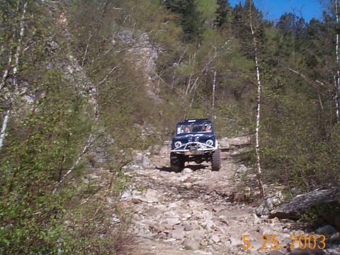 1977 Ford Bronco - A 1977 Ford Bronco navigates a challenging rocky terrain on a wooded mountainside.