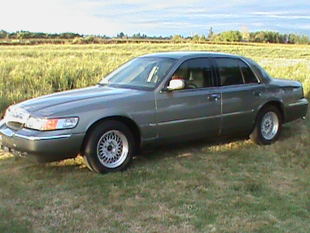 Gray Mercury Grand Marquis sedan parked on grass beside a field