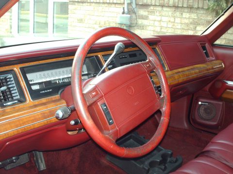 1991 Mercury Grand Marquis - The interior of a 1991 Mercury Grand Marquis features red upholstery, wood grain accents, and a prominent steering wheel.