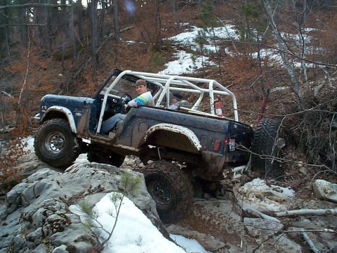 1977 Ford Bronco - A mud-caked blue topless early Ford Bronco with a white exterior roll cage, no doors and a red fire extinguisher mounted behind the seats w…