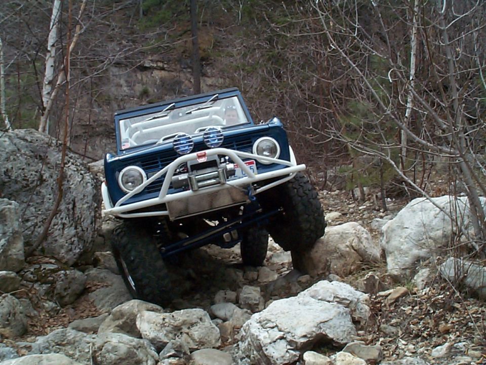 Blue off-road SUV with a white bumper and winch navigating rocky terrain