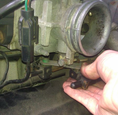 1991 Mercury Grand Marquis - Close-up of a throttle body assembly with a hand holding a sensor, showing linkage and electrical connectors.