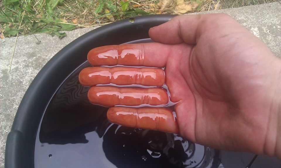 Hand with fingers in dark fluid in a black pan, Supermotors.net logo visible