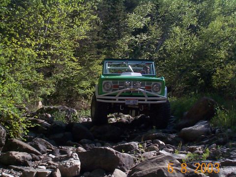1977 Ford Bronco - 1977 Ford Bronco tackling a challenging rocky trail in a wooded area.