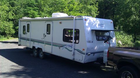1989 Ford Bronco - A white travel trailer is parked on a paved surface, with a pickup truck attached to its hitch.
