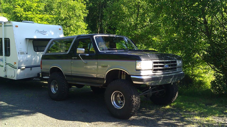 Lifted black and silver Ford Bronco on mud tires parked next to a Prowler travel trailer