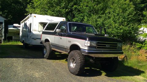 1989 Ford Bronco - A lifted Ford Bronco is parked next to a travel trailer in a wooded area.