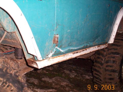 1977 Ford Bronco - Close-up of a teal SUV's side panel, revealing rust and damage near the rocker panel and fender flare.