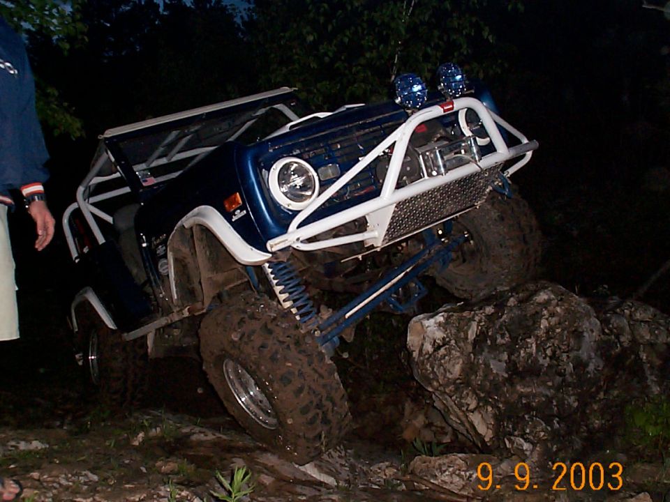 Blue 1977 Ford Bronco off-roading over rocks with white roll cage