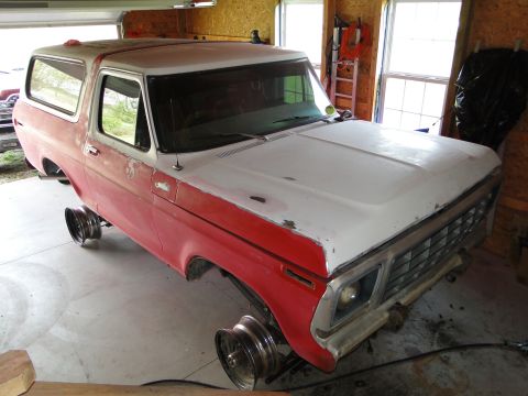 1978 Ford Bronco - A red and white 1978 Ford Bronco is shown in a garage, missing its wheels and undergoing restoration.