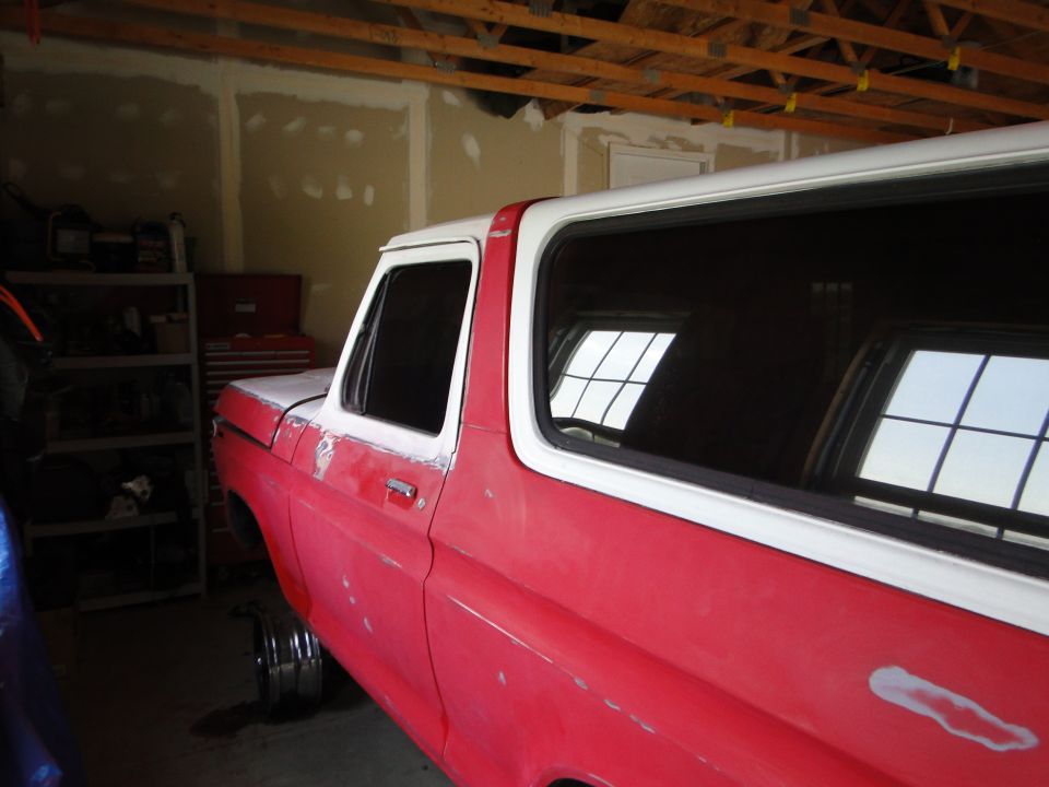 Side view of a red and white 1978 Ford Bronco undergoing restoration
