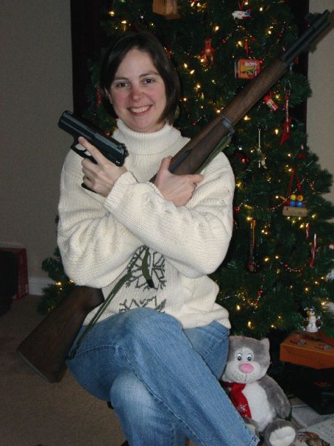 2003 Ford Crown Victoria - Woman poses with firearms near a Christmas tree, holding a pistol and a rifle.