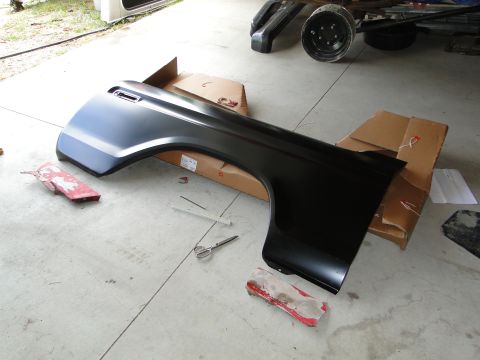 1978 Ford Bronco - A black fender part is laid out on cardboard boxes in a garage, with tools and rags scattered around.