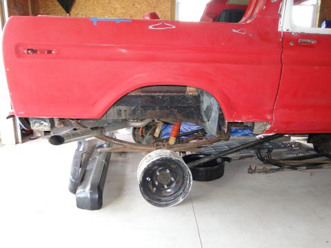 1978 Ford Bronco - Rear suspension and bodywork of a red Ford Bronco are exposed while it's raised on jack stands for maintenance.