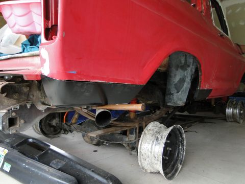 1978 Ford Bronco - The rear suspension and axle of a red 1978 Ford Bronco are visible, along with a detached wheel and exhaust pipe.