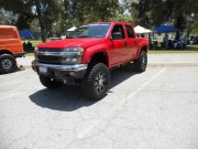 1986 Ford Bronco - A red Chevrolet Colorado pickup truck is parked in a lot with trees and tents in the background.