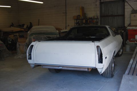1975 Ford Ranchero - A white Ford Ranchero is undergoing repairs in a workshop, with another vehicle covered in the background.
