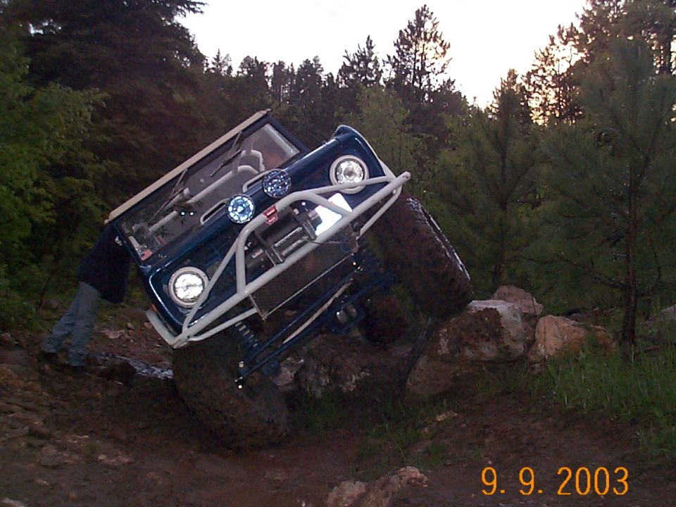 Blue 1977 Ford Bronco with winch and roll cage navigating rocks
