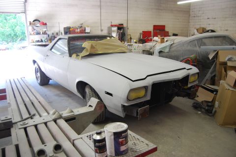 1975 Ford Ranchero - A white Ford Ranchero is undergoing repairs in a workshop, with another vehicle covered in plastic in the background.