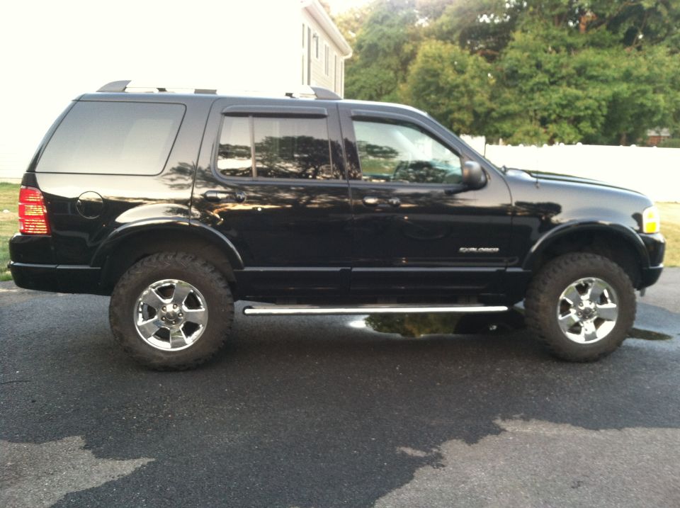 Black Ford Explorer SUV parked on asphalt, side view. Chrome wheels and running boards are visible