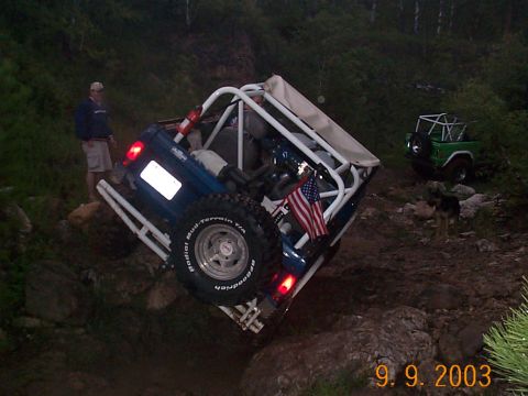 1977 Ford Bronco - Two off-road vehicles navigate challenging rocky terrain, with a person and a dog observing the action.