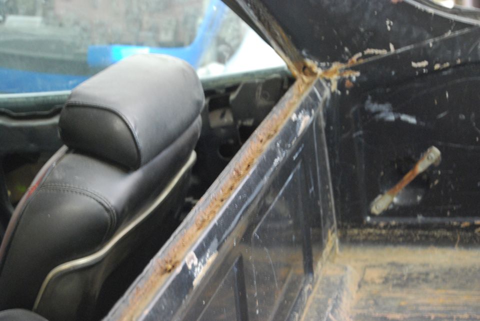 Interior view of a vehicle showing a black seat and rusty metal trim around the window frame