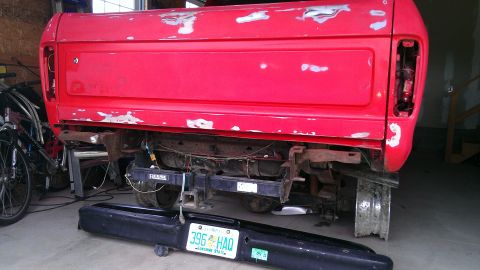 1978 Ford Bronco - Rear view of a red pickup truck bed undergoing repairs, with a detached bumper and license plate visible.