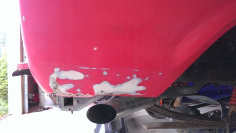 1978 Ford Bronco - Close-up of a red vehicle's rear quarter panel showing body filler work and an exhaust pipe.