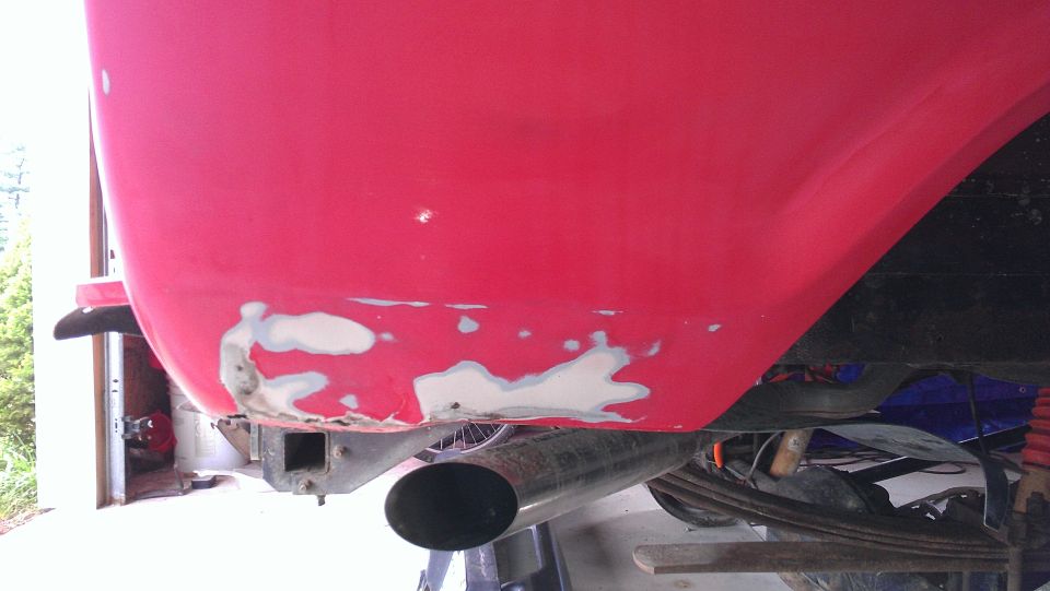 Red vehicle rear quarter panel with body filler and exhaust pipe