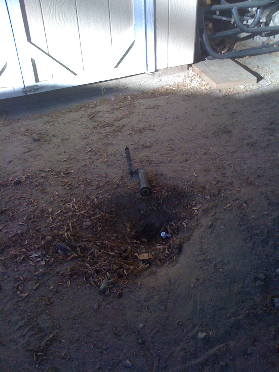 Sprinkler head emerging from disturbed soil and leaves near a white garage door