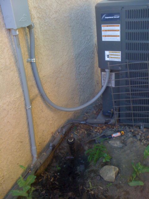 1968 Ford Mustang - Exterior view of an AC unit, conduit, and sprinkler system components against a wall.