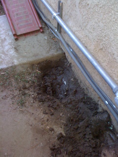 1968 Ford Mustang - A trench has been dug along the side of a building, exposing dirt and some pipes.