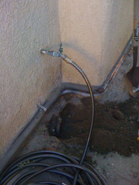 1968 Ford Mustang - A partially dug hole reveals sprinkler system components, with a faucet and hose attached to the wall.