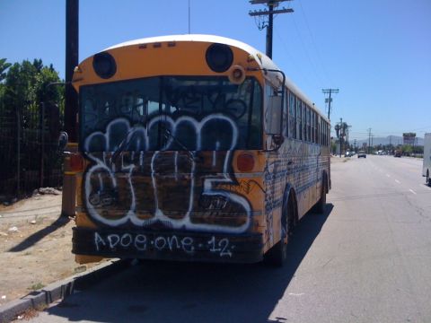 1968 Ford Mustang - A graffiti-covered school bus sits parked on the side of a highway under a clear blue sky.