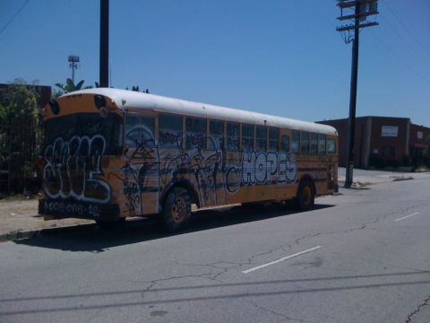 1968 Ford Mustang - A yellow school bus, covered in graffiti, sits parked on the side of a street under a clear blue sky.
