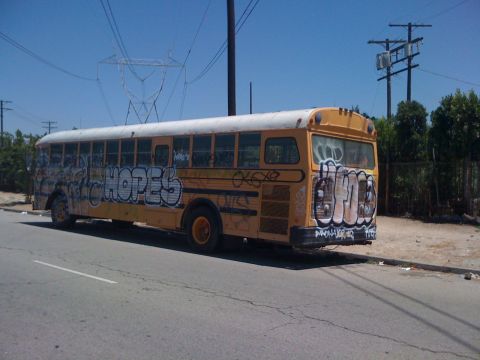 1968 Ford Mustang - A graffiti-covered yellow school bus sits parked on the side of a road under a clear blue sky.