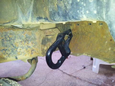 1986 Ford Bronco - A close-up view of a black tow hook mounted to a heavily rusted vehicle frame.