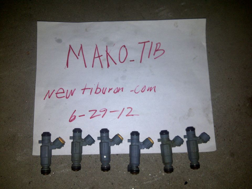 Six fuel injectors laid out on a concrete surface with a handwritten note that says MAKO-TIB, new tiburon -com, 6-29-12